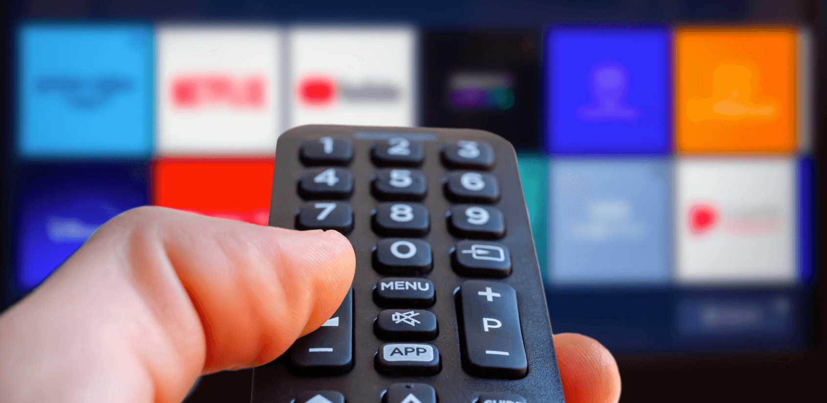 Close up of a hand holding a remote aimed at a TV screen with multiple streaming service options.