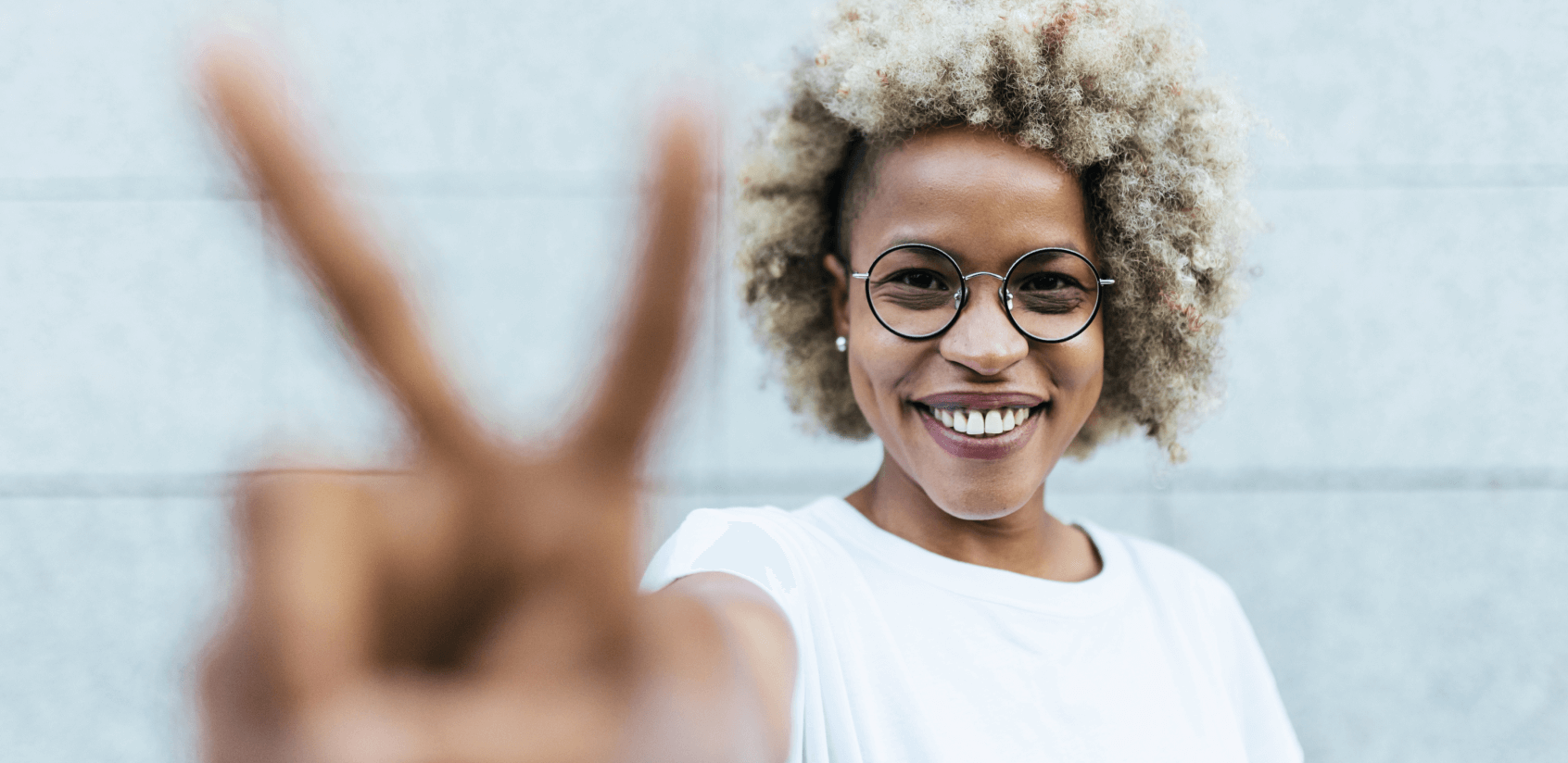 Woman smiling while reaching out her arm and making a peace sign with her fingers.