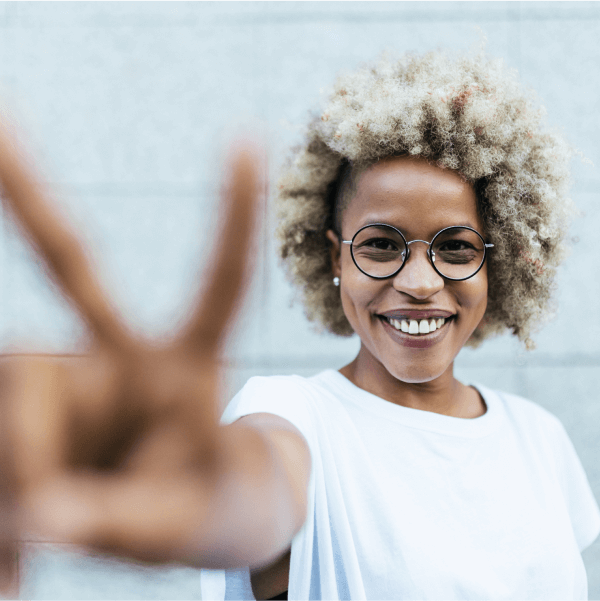 Woman smiling while reaching out her arm and making a peace sign with her fingers.