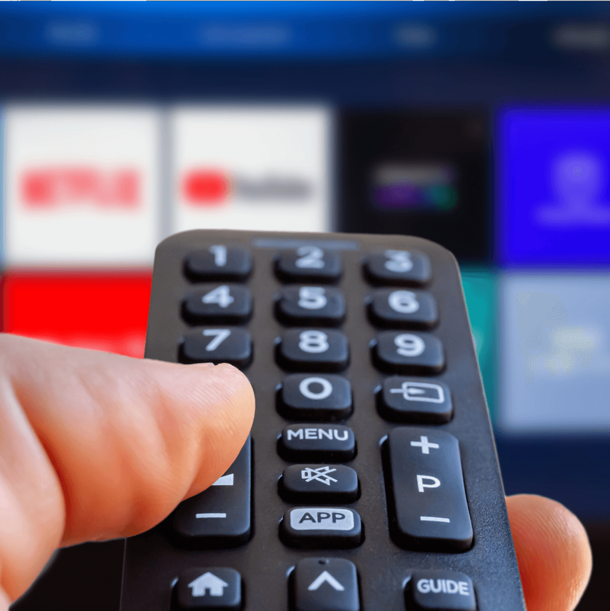 Close up of a hand holding a remote aimed at a TV screen with multiple streaming service options.